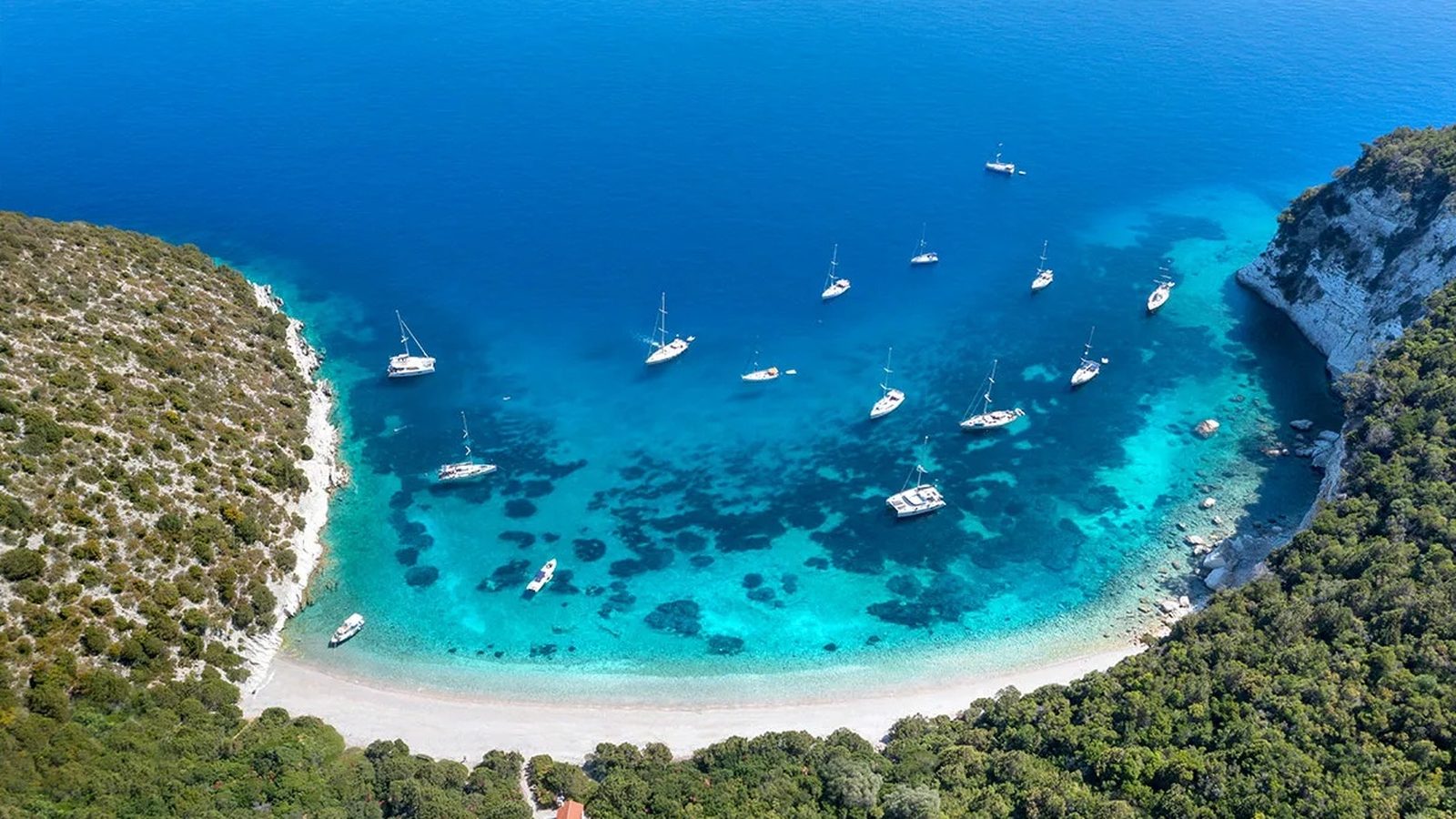 One House Bay on Atokos from the air: white pebble beach and yachts at anchor over turquoise water