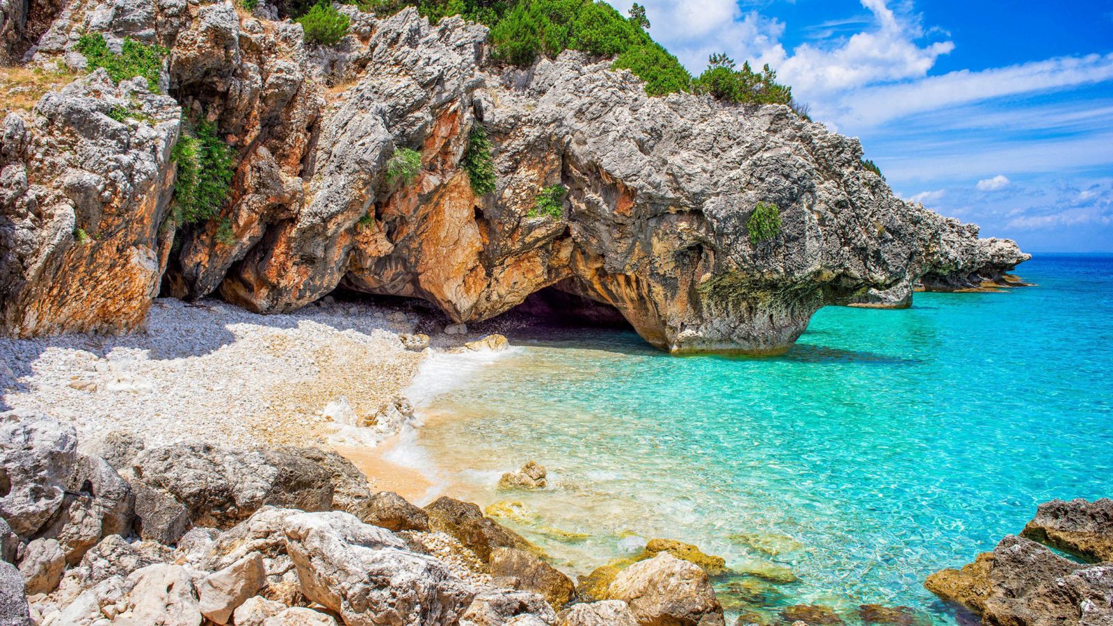 Kato Lagadi beach south of Poros: white pebbles, a rock overhang and turquoise shallows