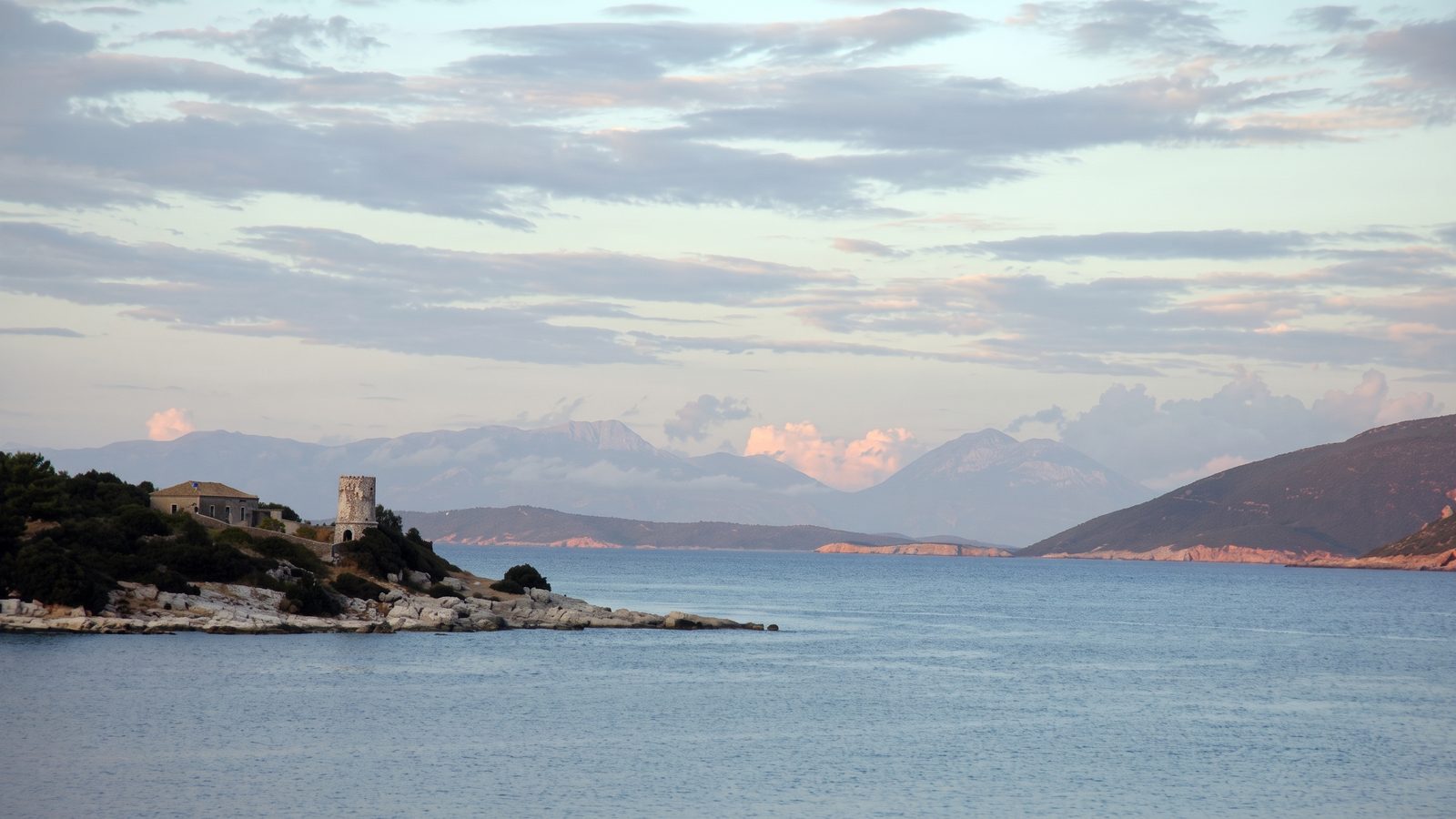 An old stone lighthouse on a headland at dusk, the mainland mountains behind
