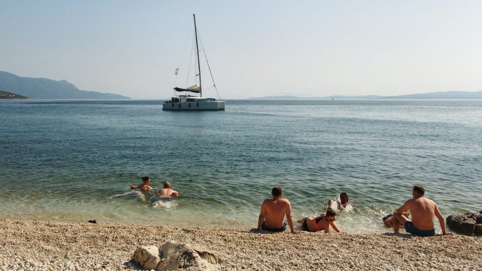 Last swim stop: the catamaran at anchor off a white pebble beach, the group in the water