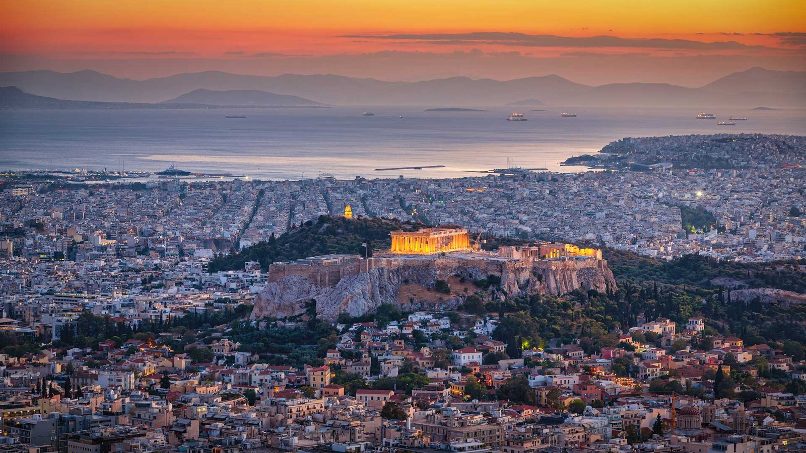 Athens at sunset from above: the lit Acropolis, the city and the Saronic Gulf beyond