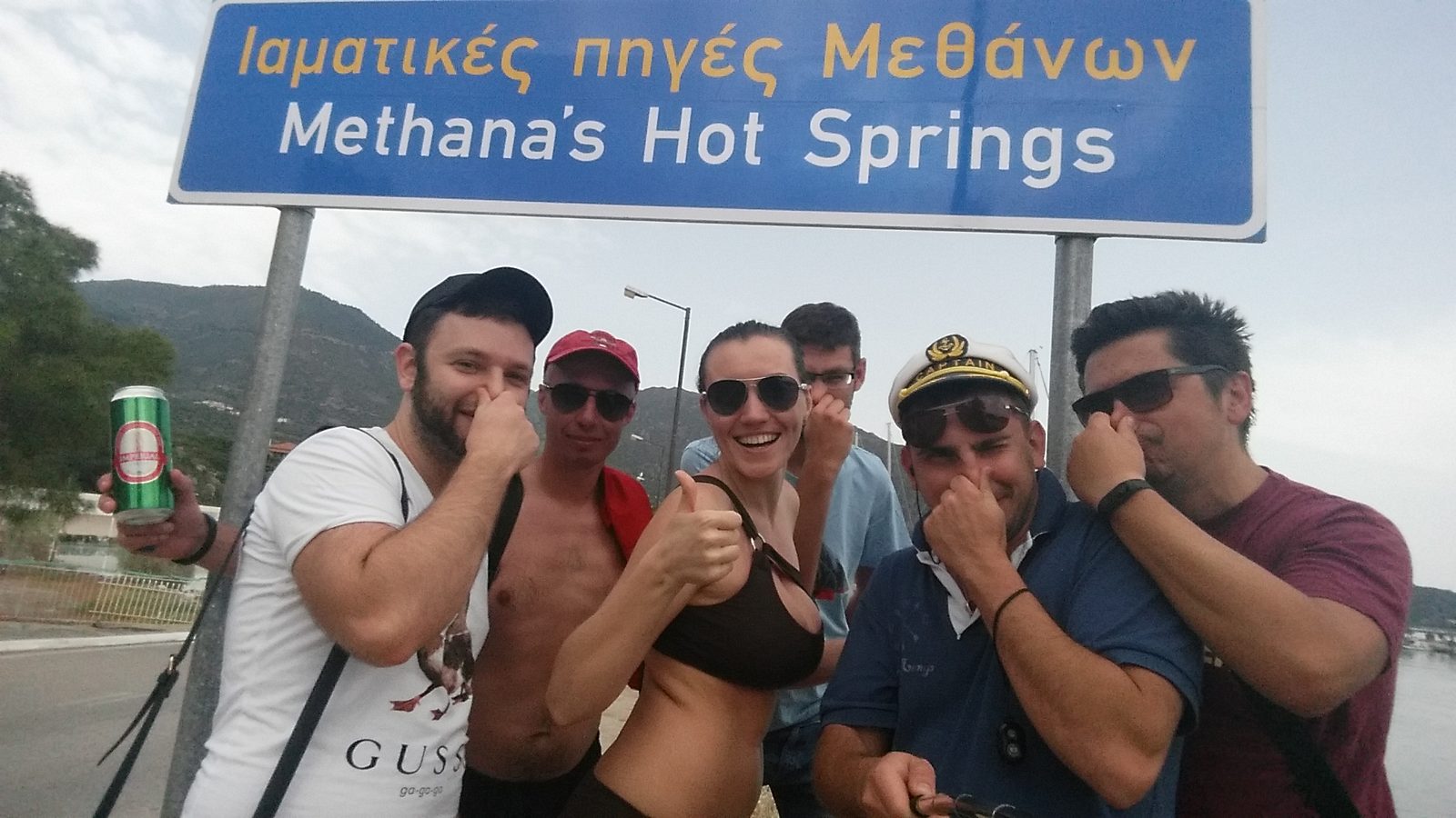 The group holding their noses under the Methana&rsquo;s Hot Springs sign, skipper in his captain&rsquo;s cap