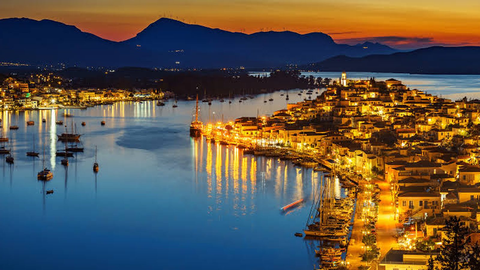 Poros harbour lit up at dusk, the mountains of the Peloponnese behind