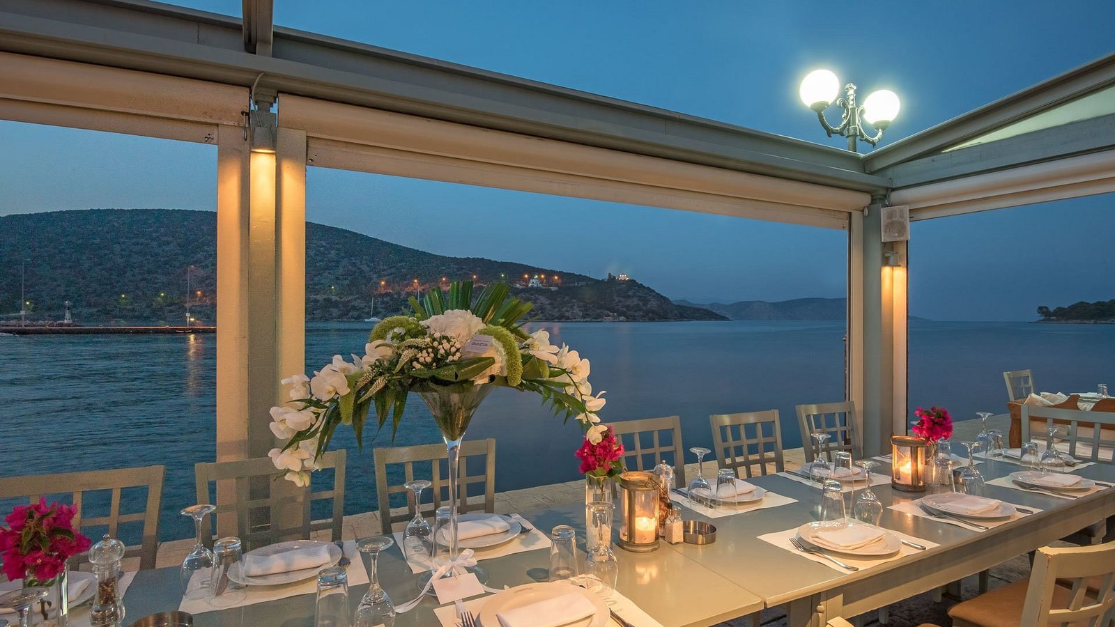 A long table set for dinner on a harbourside terrace at dusk